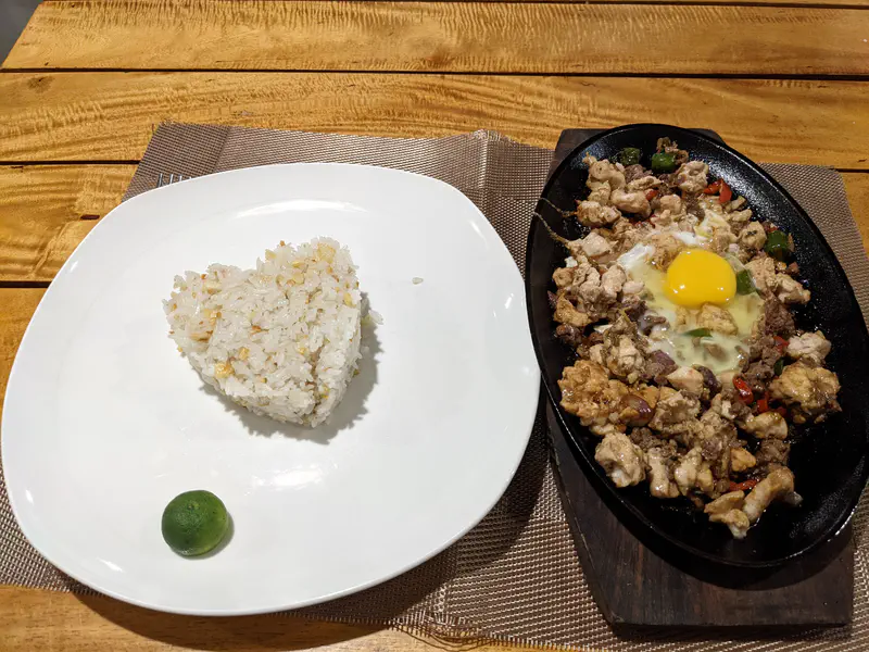 Plate of garlic rice with calamansi beside sizzling sisig topped with raw egg.