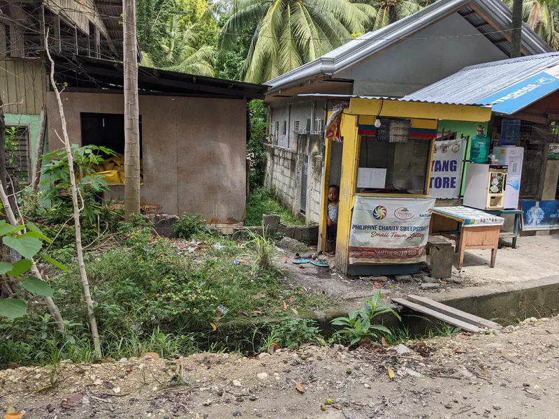 Young child standing in the doorway of a small roadside store with lottery signage.