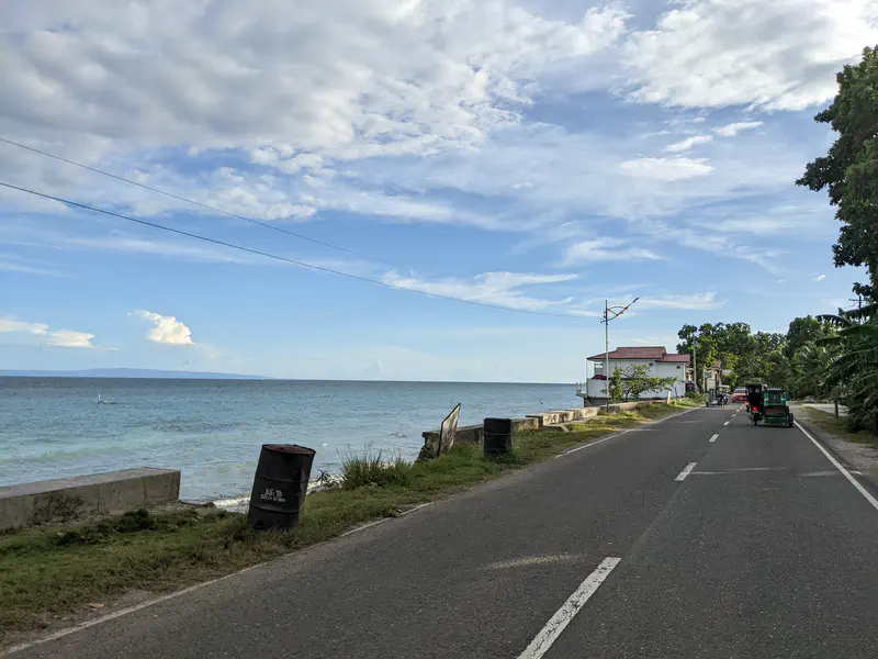 Paved road running along the shoreline with tricycles and a house facing the sea.