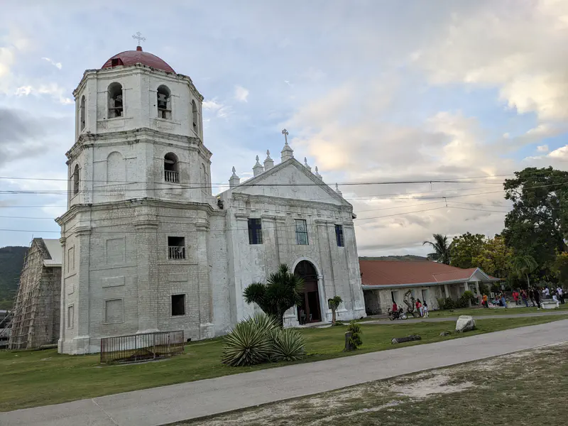 Historic white stone church with a bell tower and red dome beside a courtyard.