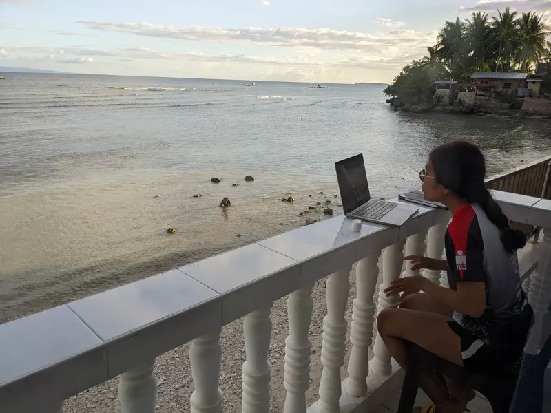 Person using a laptop while sitting on a balcony above the shoreline.