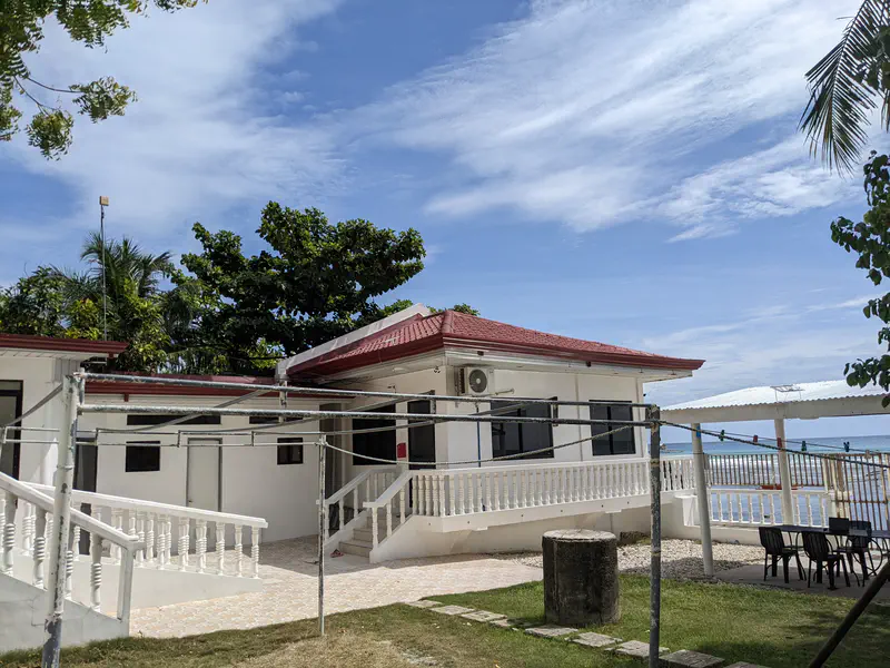 White house with red roof, outdoor seating, and view of the sea under a blue sky.