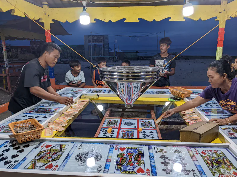 People playing a card-themed betting game with money and tokens at a fair.