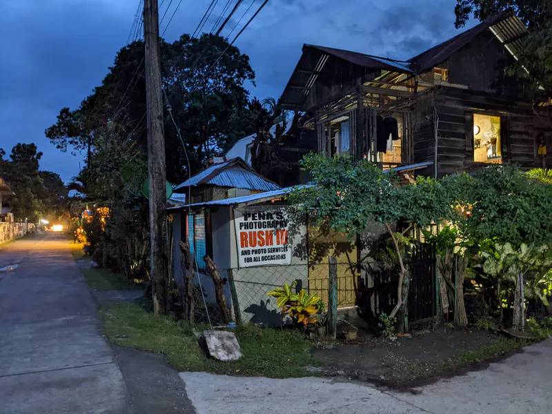 Small roadside photography shop with a wooden house above it lit at dusk.
