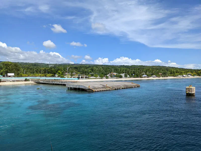 Concrete pier extending into clear blue water with a tropical island shoreline in the background.