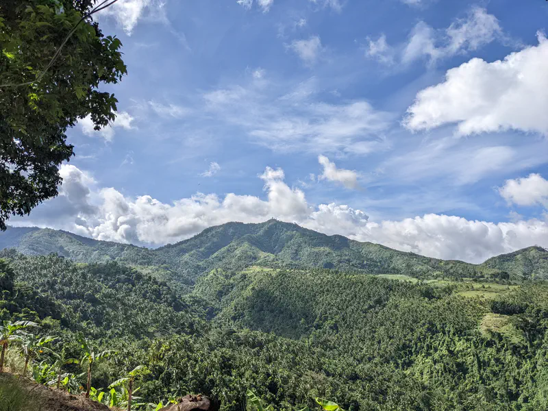 Lush green mountains under a bright blue sky with scattered clouds.
