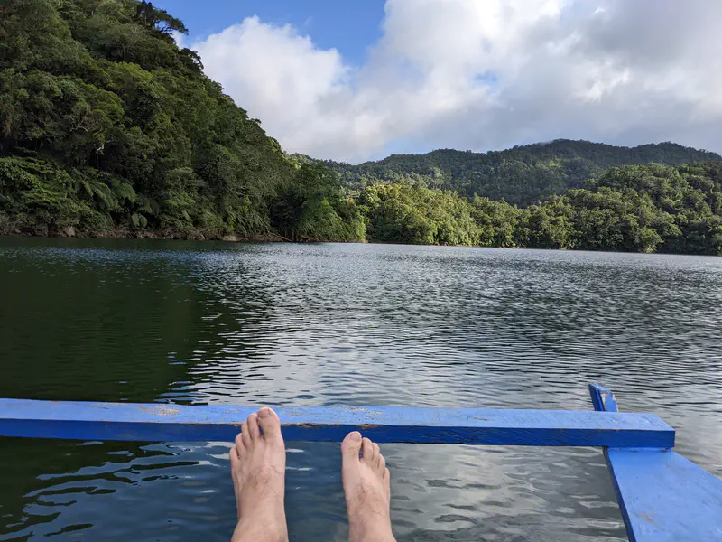 View from a boat showing feet resting on the edge with a calm lake and forested hills.