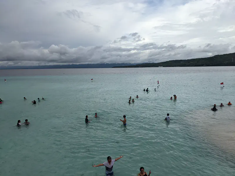 Groups of people swimming and playing in shallow turquoise water near the shore.