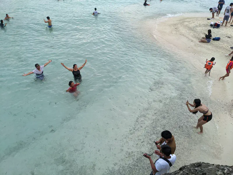 People enjoying the water and taking photos along a sandy beach with gentle waves.