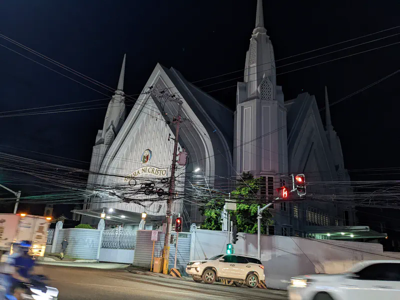 Large white church building with tall spires lit up at night near a busy intersection.