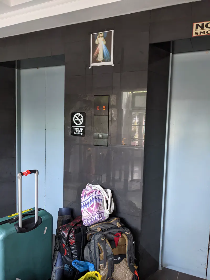 Stack of luggage and bags placed in front of two elevators with a religious image above.