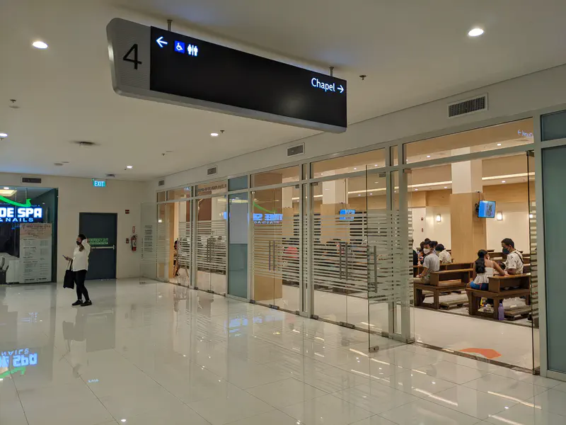 Glass-walled chapel inside a shopping mall with people seated on pews.