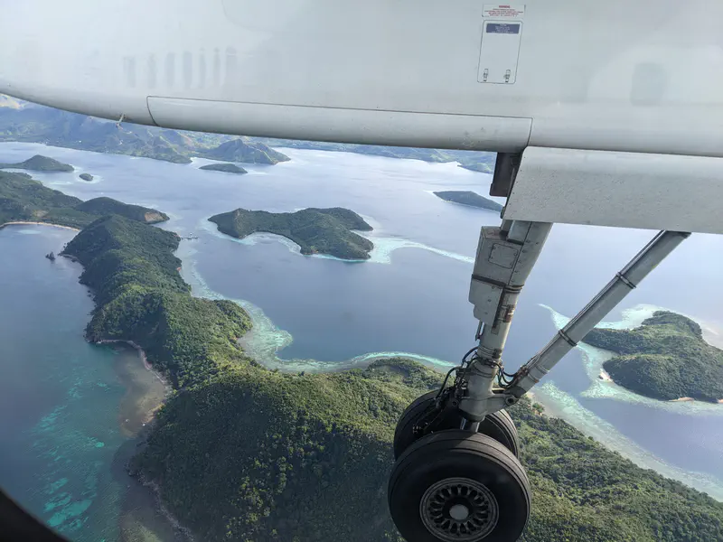 Aerial view of lush green islands surrounded by turquoise waters, with an airplane wing and landing gear in the foreground.
