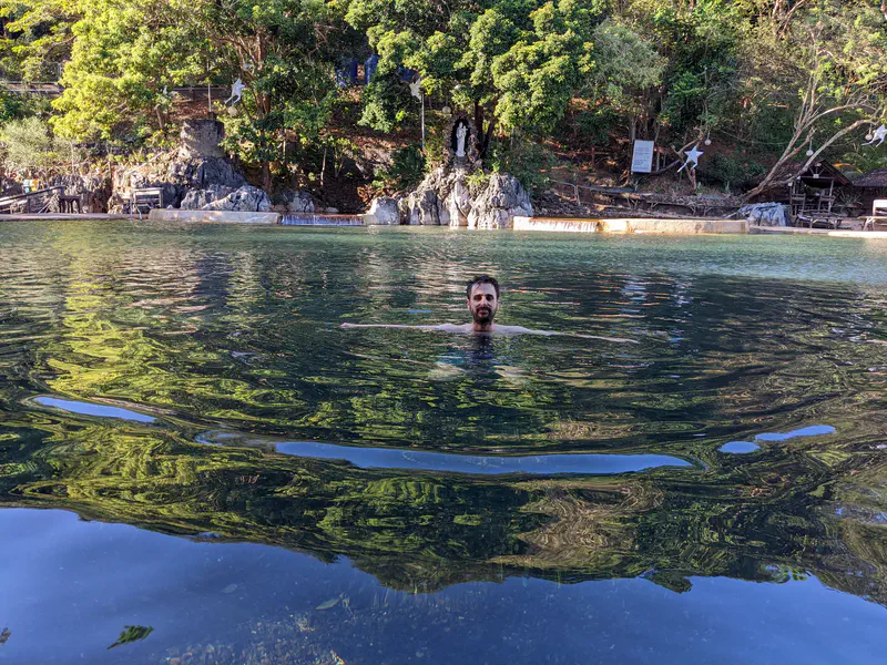 Man swimming in a calm outdoor pool surrounded by trees and rocks.