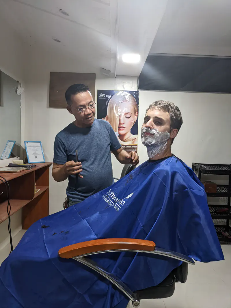 Barber preparing to shave a man with shaving cream on his face in a salon.