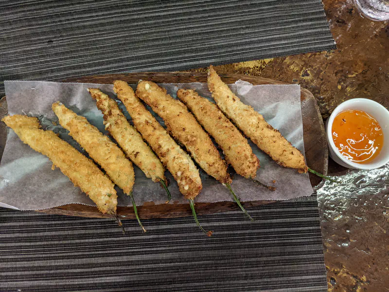 Plate of deep-fried stuffed chili peppers served with a dipping sauce.