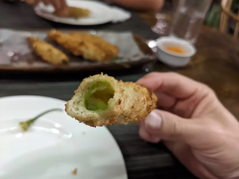 Close-up of a bitten deep-fried stuffed chili pepper showing green filling inside.