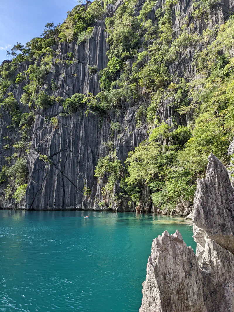 Turquoise lagoon at the base of steep limestone cliffs with greenery.