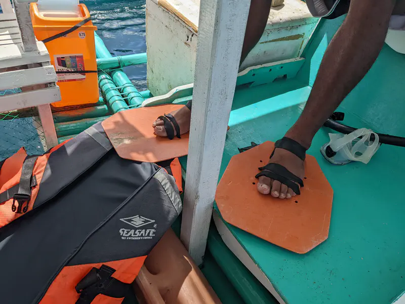 Person wearing improvised orange wooden sandals with straps on a boat deck beside a life jacket.