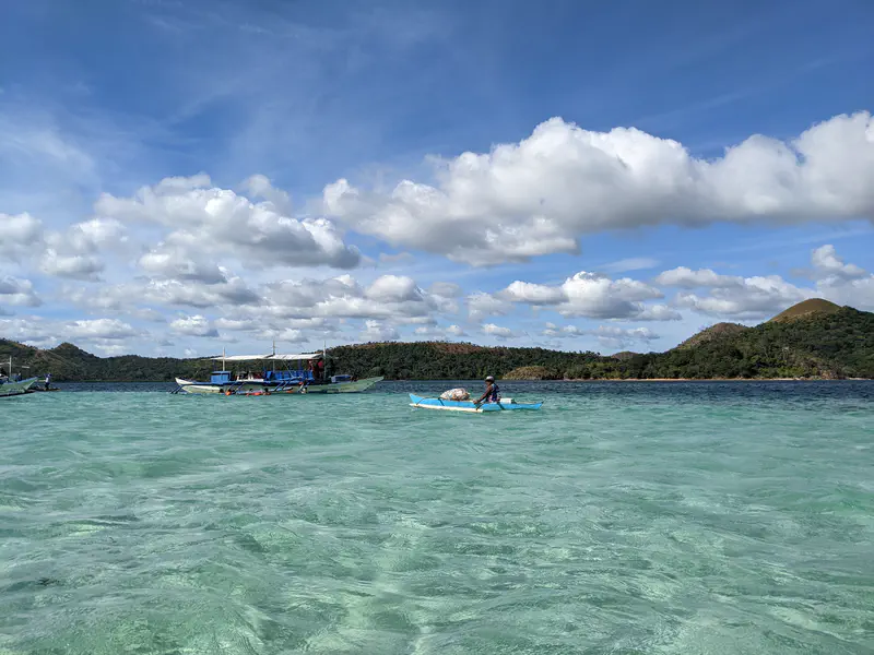 Small boats floating on turquoise water near green islands under a partly cloudy sky.