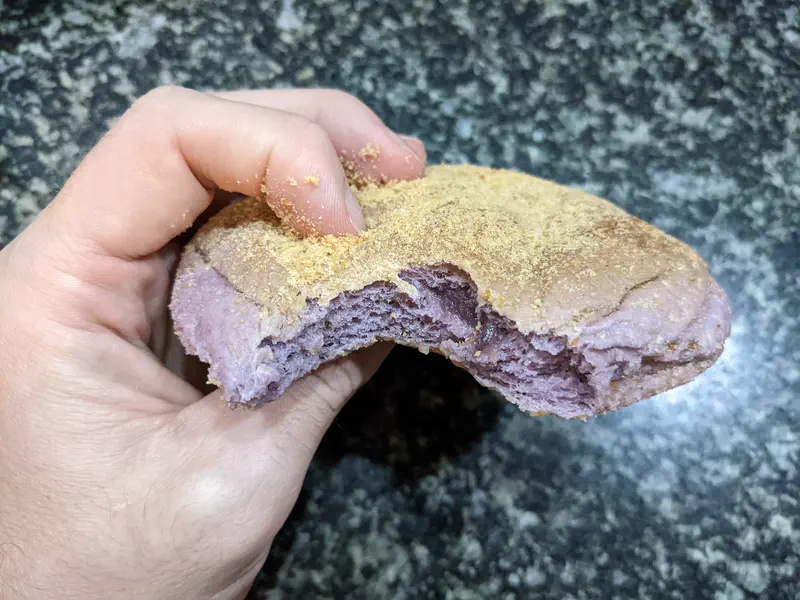 Hand holding a bitten ube cheese pandesal showing its purple interior.
