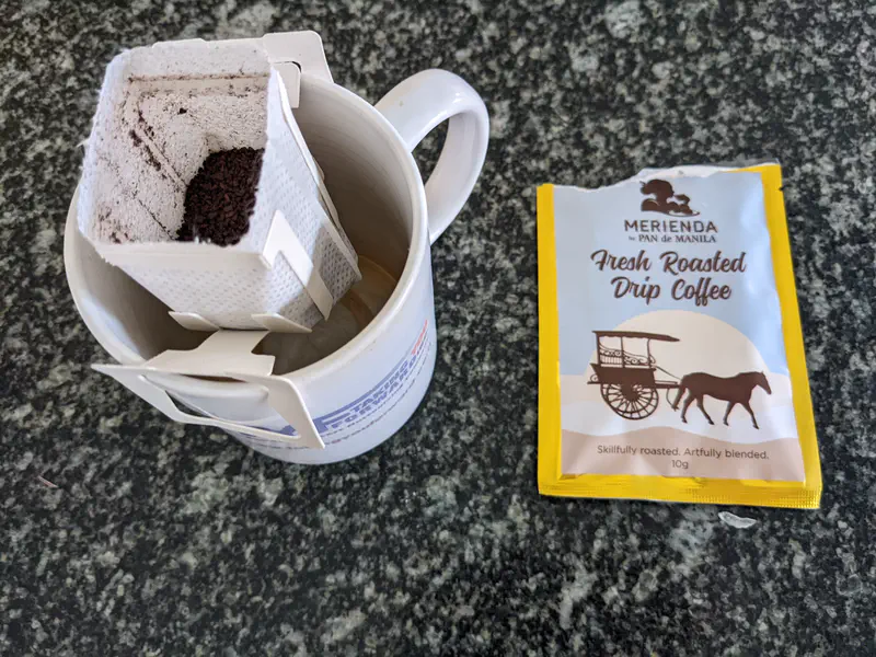 Mug with drip coffee filter and Pan de Manila fresh roasted drip coffee packet beside it.