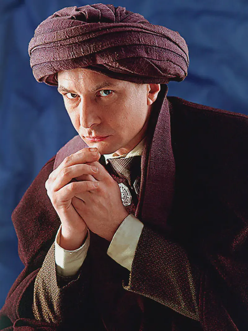 Man wearing a purple turban and cloak with a cautious expression and hands clasped together.