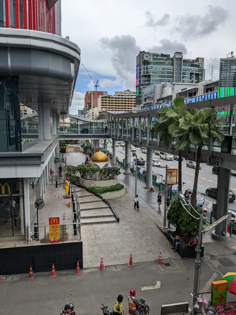 Bangkok street view with shopping mall, McDonald's, elevated walkway, palm trees, and traffic in the background.