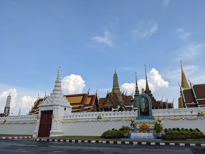 Wat Phra Kaew and the Grand Palace in Bangkok with ornate spires and white walls under a clear sky.