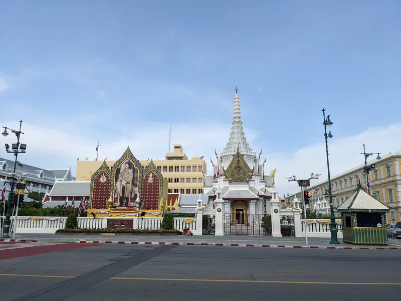 White temple shrine in Bangkok with a large portrait of the king displayed prominently beside it.