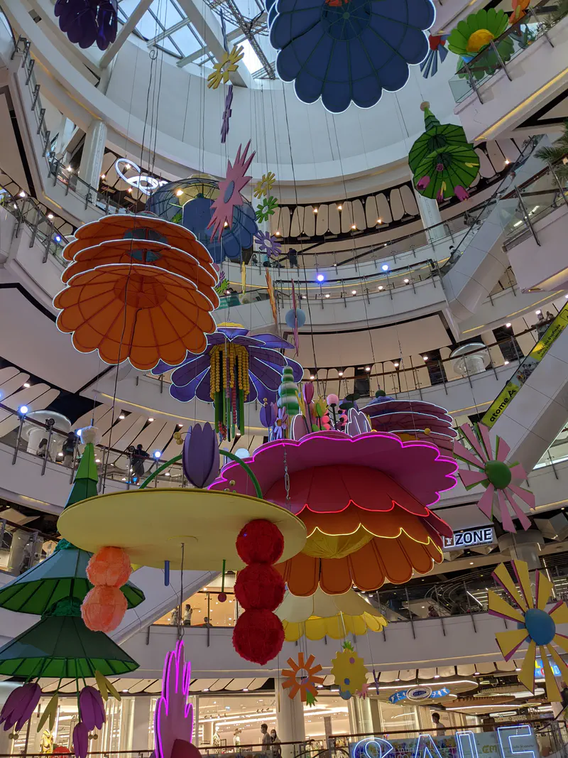 Colorful flower-shaped decorations hanging inside a multi-story shopping mall atrium.