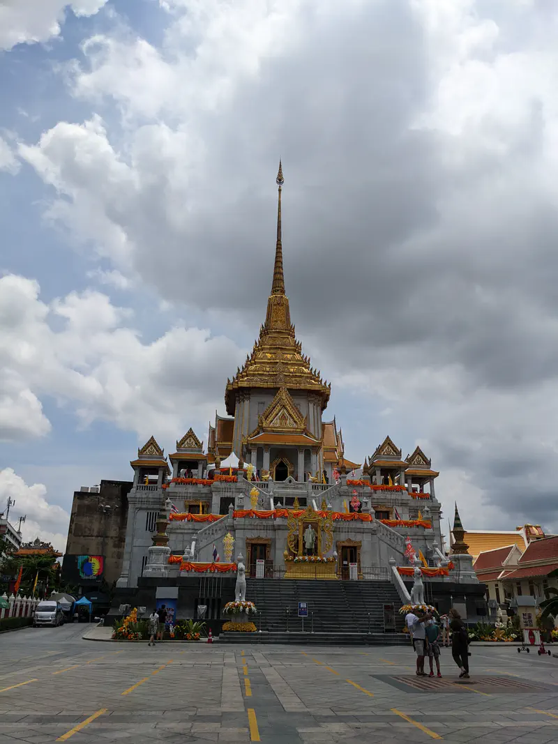Wat Traimit in Bangkok, a grand temple with golden spire and ornate decorations under a cloudy sky.
