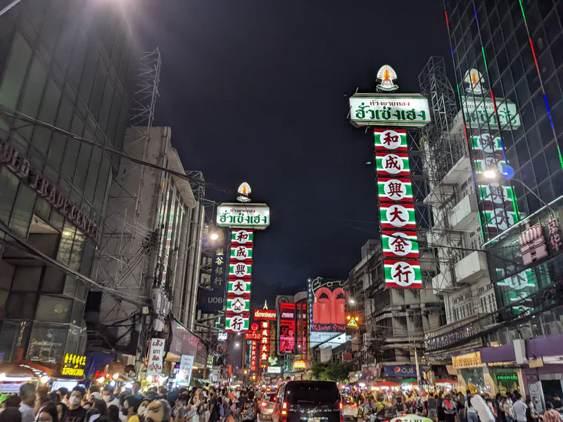 Bangkok Chinatown at night with neon signs in Thai and Chinese and bustling street crowds.