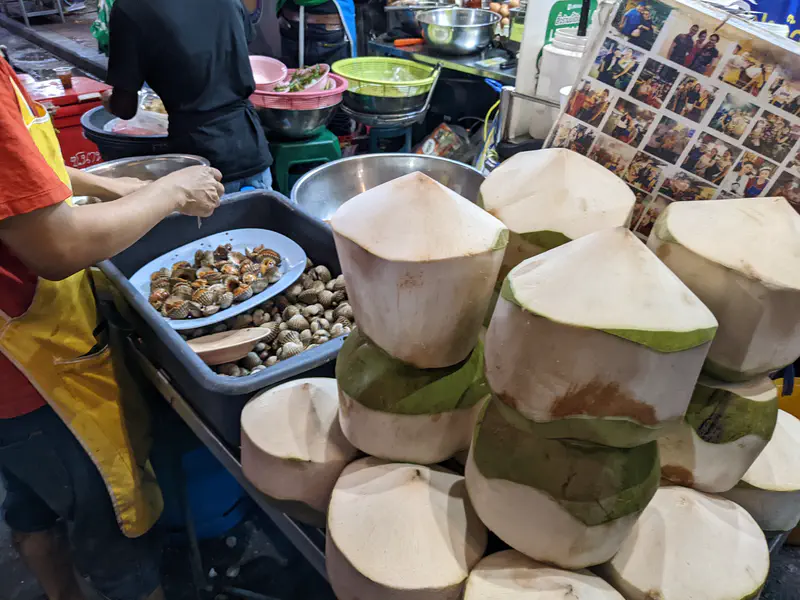 Street food vendor in Bangkok Chinatown preparing shellfish beside a stack of fresh coconuts.