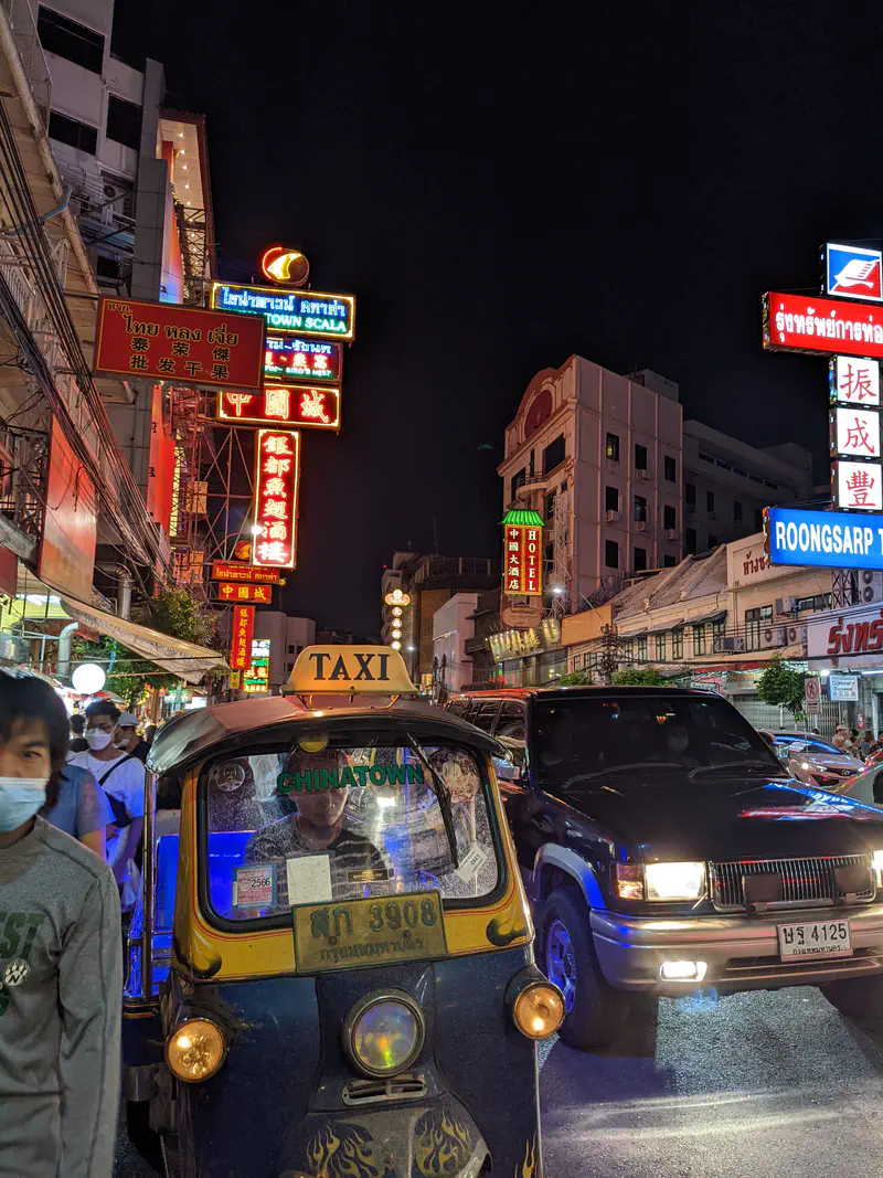 Tuk-tuk taxi in Bangkok Chinatown at night surrounded by neon signs and heavy traffic.
