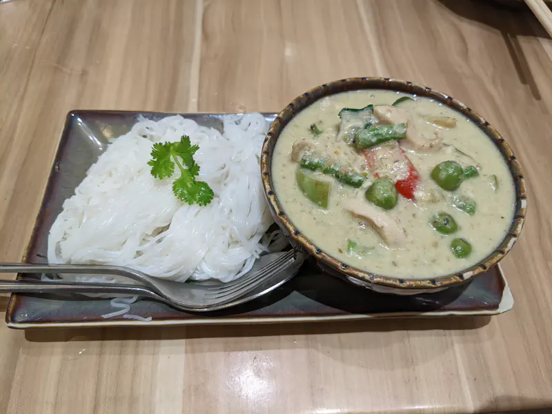 Thai green curry with chicken and vegetables served alongside rice noodles garnished with cilantro on a rectangular plate.