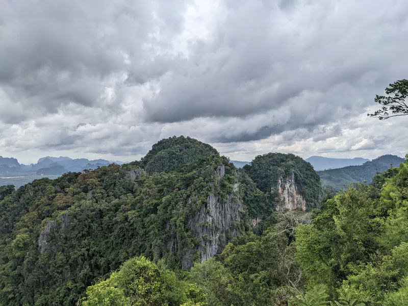 Scenic view of lush green limestone hills and distant mountains under a cloudy sky.