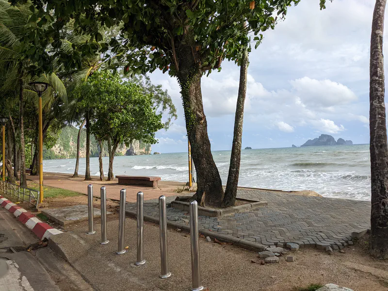 Seaside promenade shaded by trees with a view of the ocean and limestone islands in the distance.