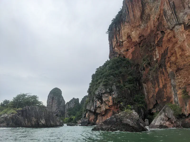 Dramatic limestone cliffs with red and gray rock faces rising above the green sea, partly covered with vegetation.