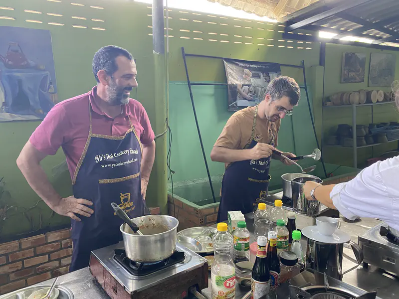 Cooking class participants wearing aprons while preparing Thai food at individual cooking stations with pots and bottles of ingredients.