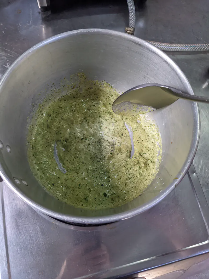 Pot of Thai green curry simmering on a stove with curry paste mixed into coconut milk.