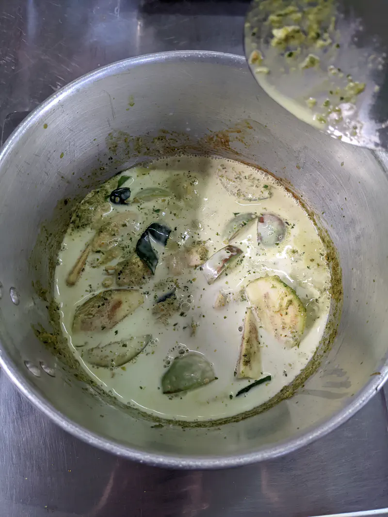 Thai green curry cooking in a pot with coconut milk, vegetables, and fresh herbs.