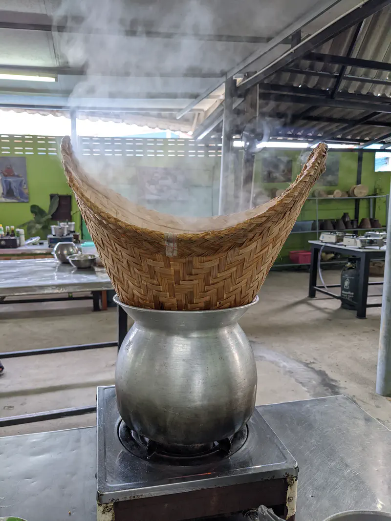 Traditional bamboo steaming basket placed over a pot with steam rising during rice preparation.