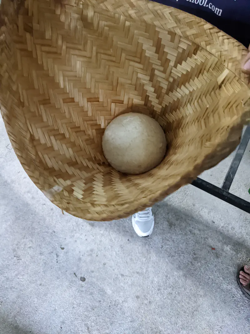 Cooked sticky rice ball inside a traditional woven bamboo steaming basket.