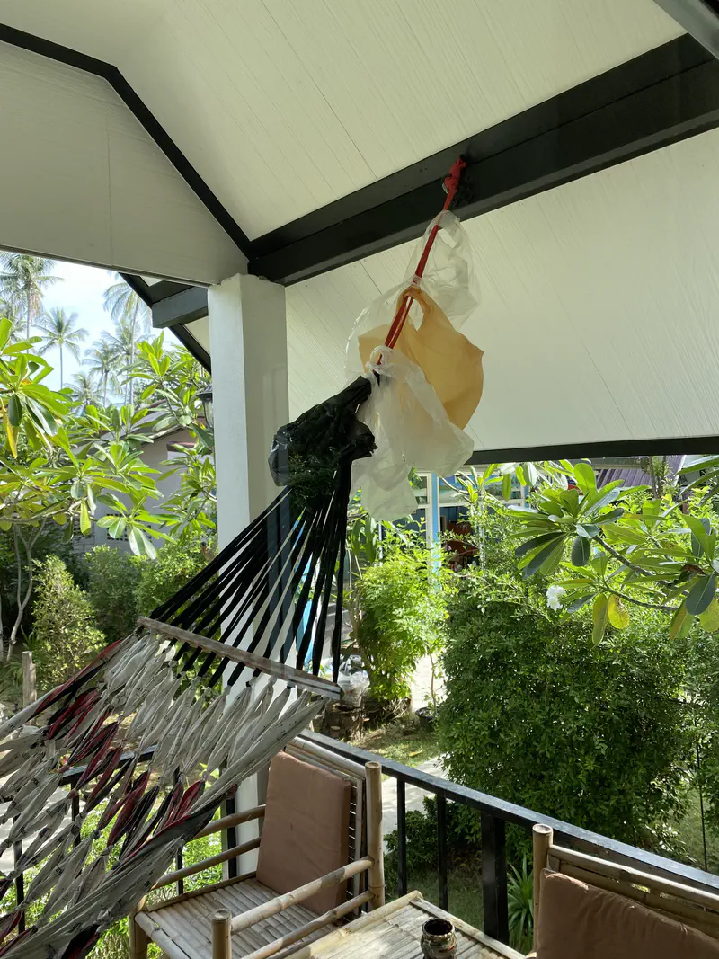 Close-up of a hammock tied to the frame of a bungalow porch with plastic bags hanging above it.