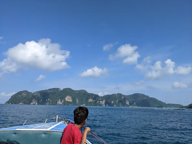 Person on a boat looking toward a lush green island under a blue sky with scattered clouds.