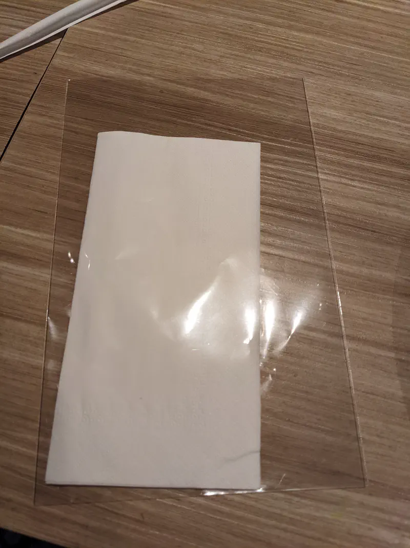 White paper napkin placed on a wooden table with a transparent plastic sheet underneath.
