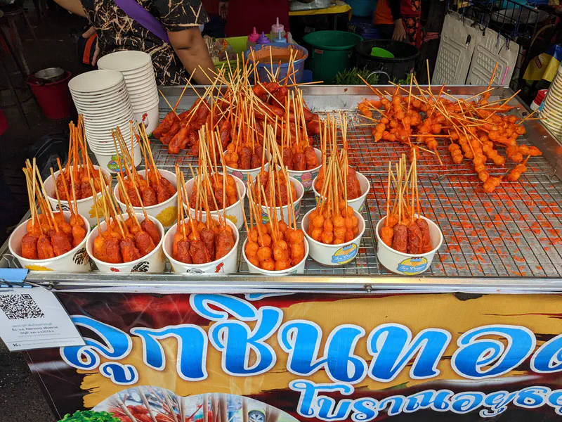 Street food stall displaying bowls filled with skewered deep-fried meatballs and sausages.