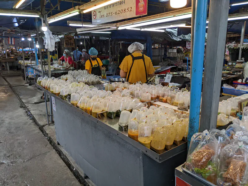 Prepared food packaged in clear plastic bags lined up on a market stall table with vendors working in the background.