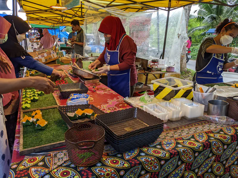 Vendors under a yellow tent preparing traditional Thai desserts at a street market stall.